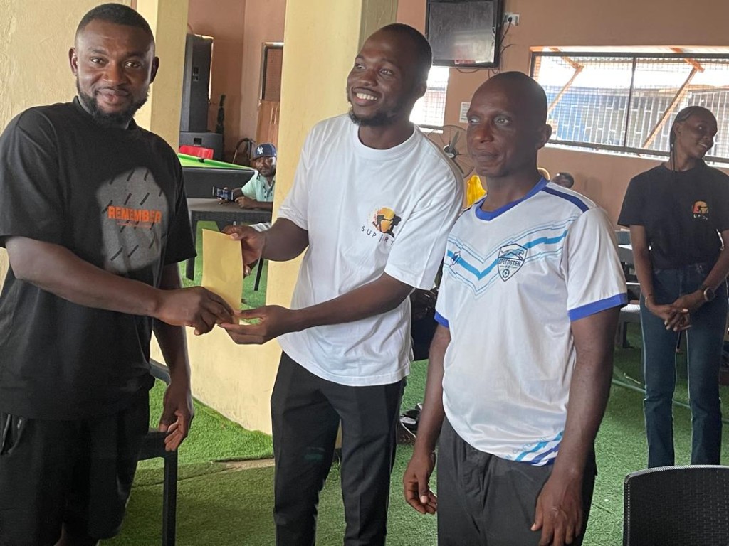 Supportz team members in branded shirts handing an envelope to a smiling member during a community meeting